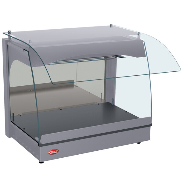 A Hatco gray curved glass food warmer on a countertop with a clear glass cover.