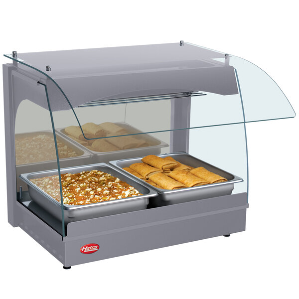 A Hatco Gray Glo-Ray curved countertop food warmer displaying food in pans with glass covers.