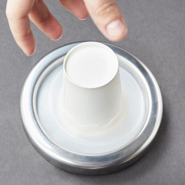 A hand reaching for a white cup on a Carlisle cup dispenser.