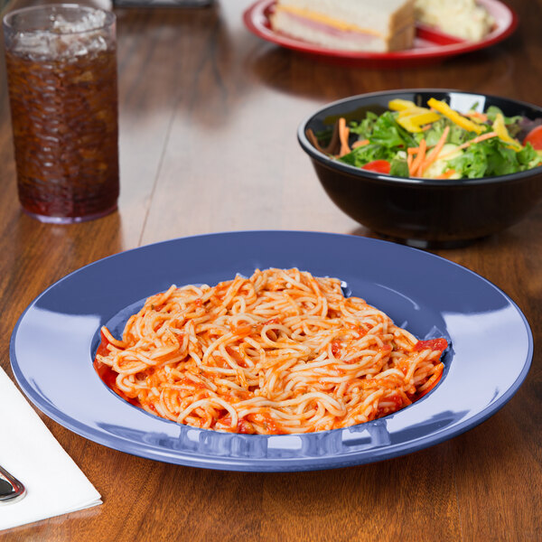 A bowl of salad with vegetables and a plate of spaghetti with sauce on a table.