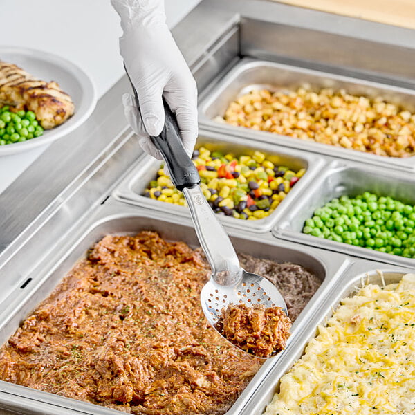 A person using a Vollrath perforated basting spoon to serve food from a metal tray.