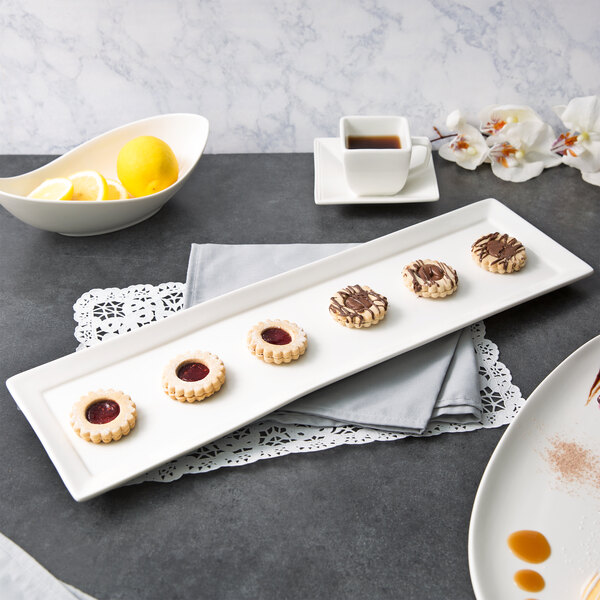 A 10 Strawberry Street white rectangular porcelain platter with cookies and a bowl of lemon wedges on it.