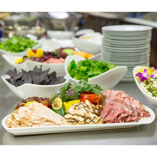 A white porcelain sword platter with a buffet of food on a table.