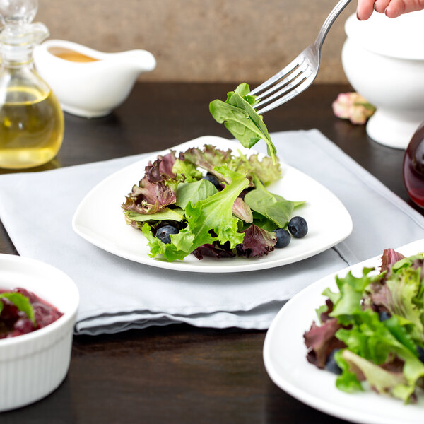 A plate of salad with a 10 Strawberry Street white triangle porcelain coupe plate with a fork.