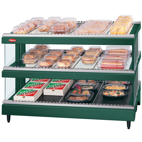 A Hunter Green Hatco heated glass food display case with shelves of food on a counter.