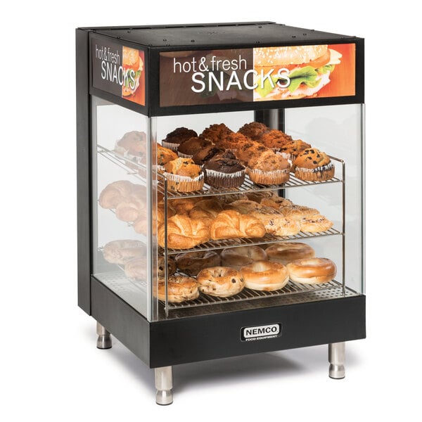 A Nemco countertop hot food display case with pastries and muffins on angled shelves.