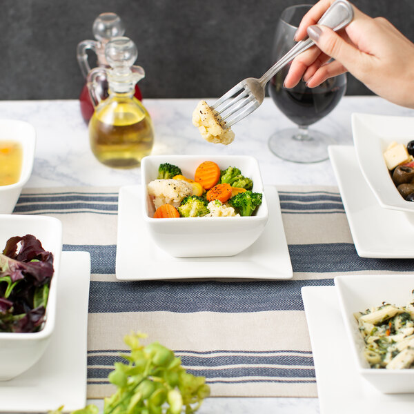 A person holding a fork over a white bowl of vegetables.