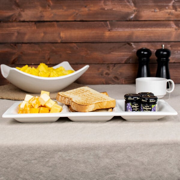 A white porcelain tray with 3 pockets holding a plate of toast, jam, and a bowl of fruit.