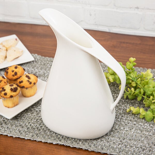 A white 10 Strawberry Street porcelain milk jug on a table with muffins.