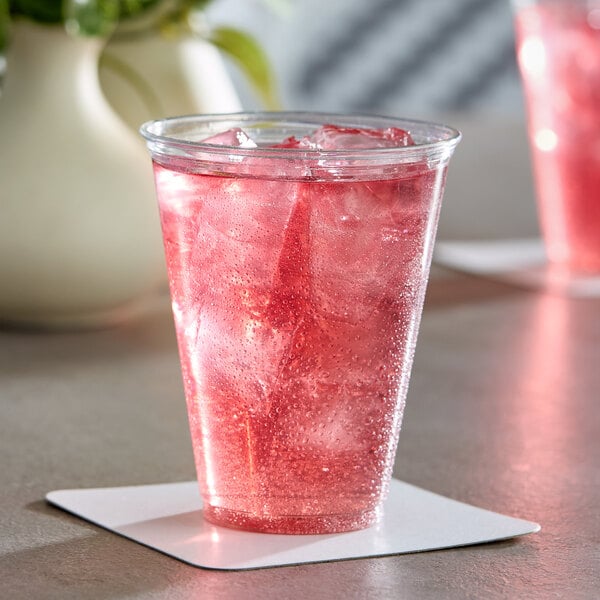 A clear plastic cup filled with a pink iced beverage, placed on a white coaster.