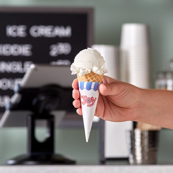 A hand holding a JOY jacketed sugar cone of ice cream.