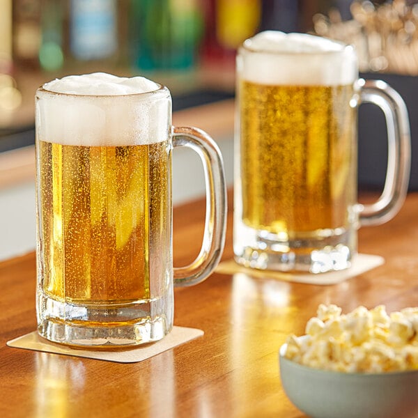 Two Libbey paneled beer mugs on a table with a bowl of popcorn.