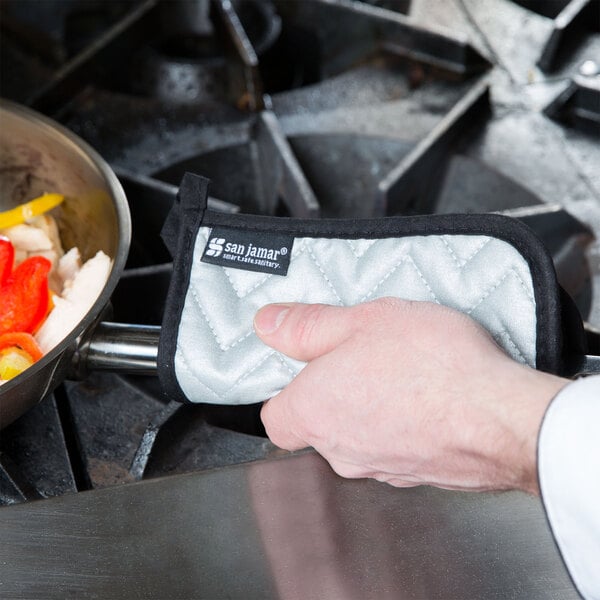 A hand using a San Jamar cotton and silicone pot holder to hold a pan of vegetables.