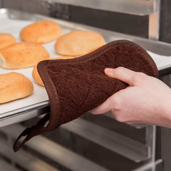 A hand using a San Jamar terry cloth pot holder to hold a tray of bread.