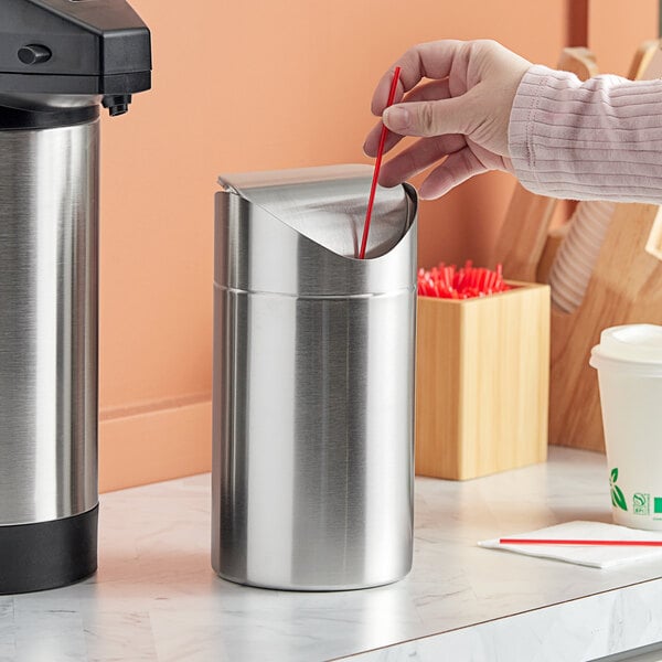 A hand placing a straw into an American Metalcraft stainless steel round swing waste bin.