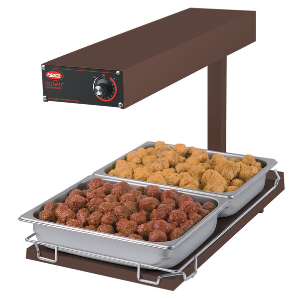 A Hatco portable food warmer with trays of meatballs and chicken on a table.