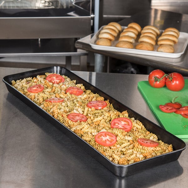 A Carlisle black fiberglass market tray with pasta and tomatoes on a counter.