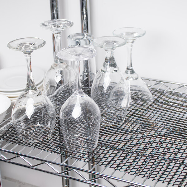 A San Jamar black shelf liner on a metal rack with wine glasses.