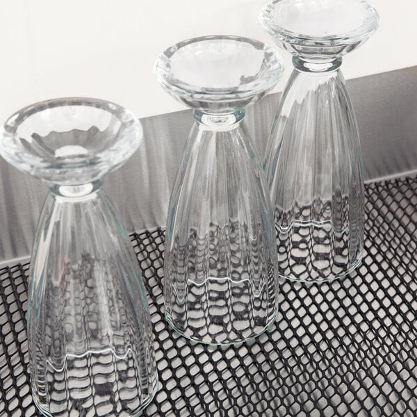 A San Jamar black shelf liner on a metal shelf holding clear glass vases.