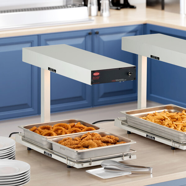 A Hatco heated shelf with trays of food on a counter.