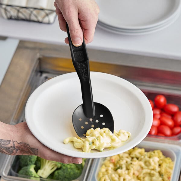 A person holding a plate with a black Camwear perforated spoon over it.