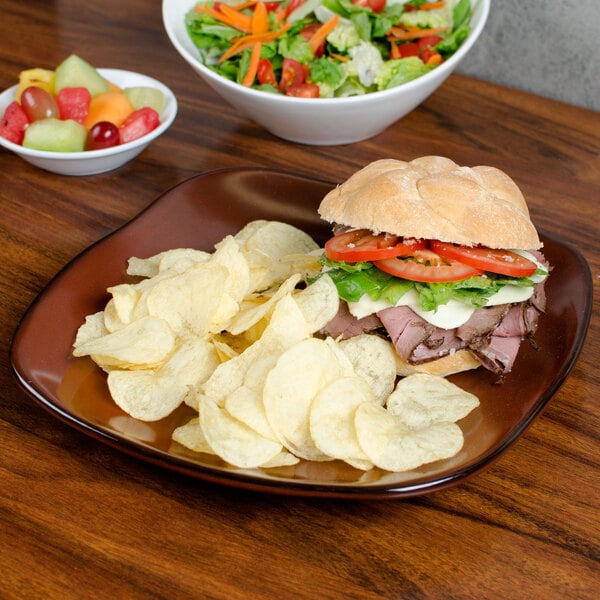 A Tuxton Artisan Red Rock square china plate with a sandwich and potato chips on a table.