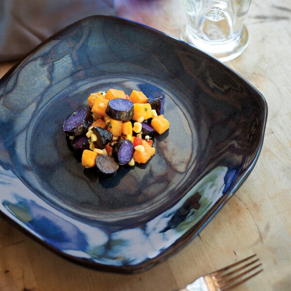 A close-up of a Tuxton Artisan Night Sky china plate of food with a fork and knife on the table.
