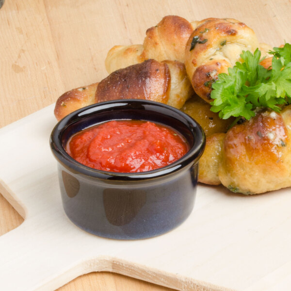 A Tuxton Artisan Night Sky china ramekin filled with red sauce next to a plate of bread.