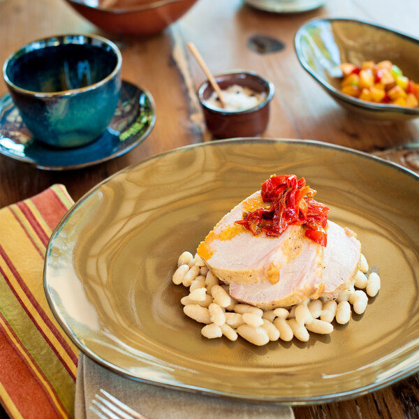 A brown bowl with a piece of meat in it and red peppers on top.