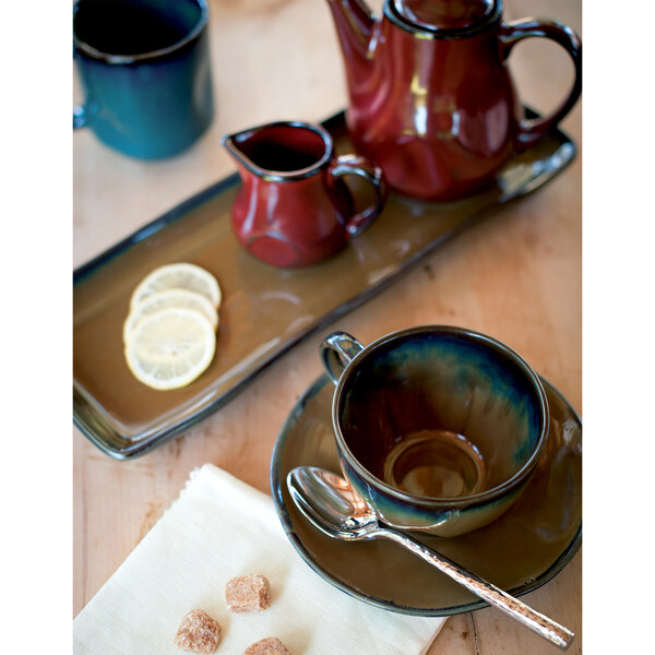 A Tuxton Mojave china saucer with a teacup and a spoon on a table.
