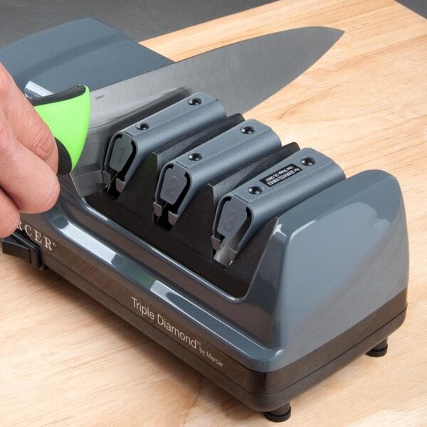 Hand pulling green-handled chef knife through a Mercer Triple Diamond electric knife sharpener