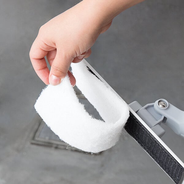 A hand holding a Unger white scrub pad.