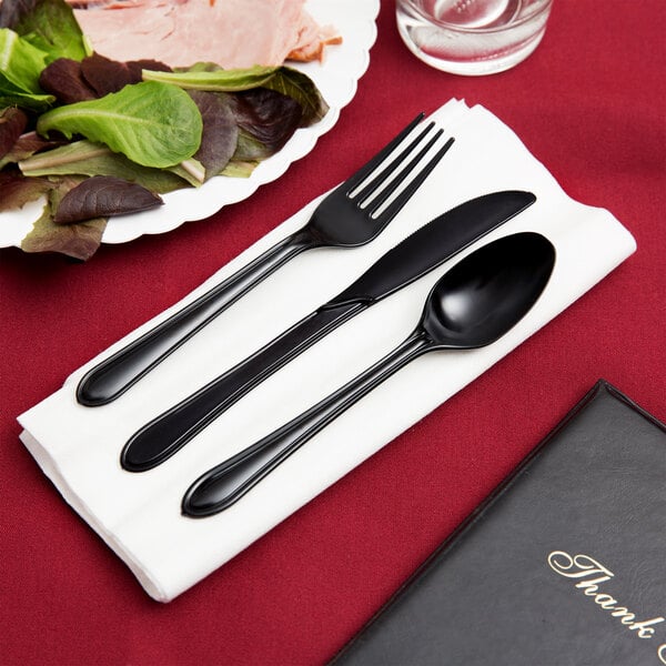 A white linen-like napkin with a black plastic fork and knife on top.