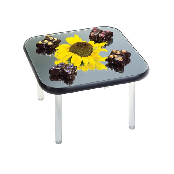 A Geneva square rimless mirror food display tray with chocolate butterflies and a sunflower on a table.