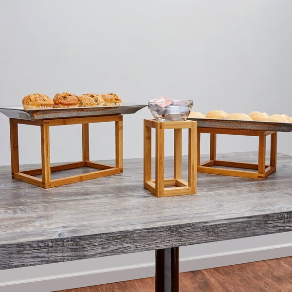 An American Metalcraft bamboo riser set with wooden trays of pastries on a table.