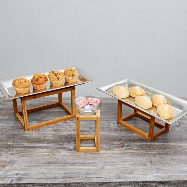 An American Metalcraft bamboo display riser set with trays of muffins and rolls on a table.