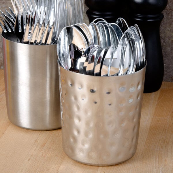 A close-up of a hammered stainless steel French fry cup filled with silverware.