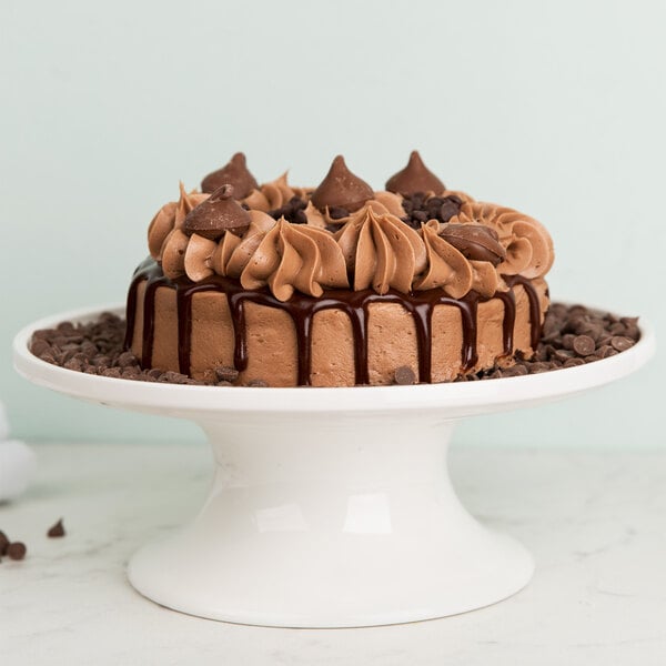 White cake stand holding a chocolate cake with chocolate chips surrounding