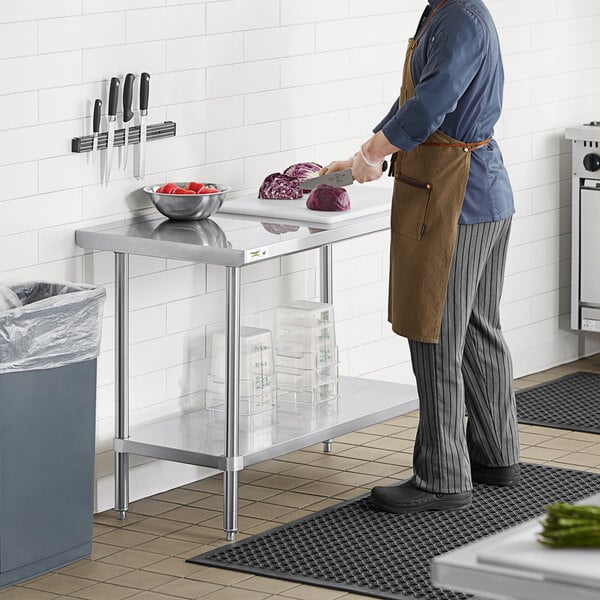 A man in a professional kitchen cutting vegetables on a Regency stainless steel work table.