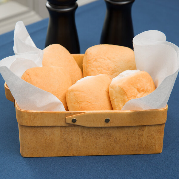 An American Metalcraft rectangular poplar wood basket filled with rolls on a table with a basket of bread and paper napkins.