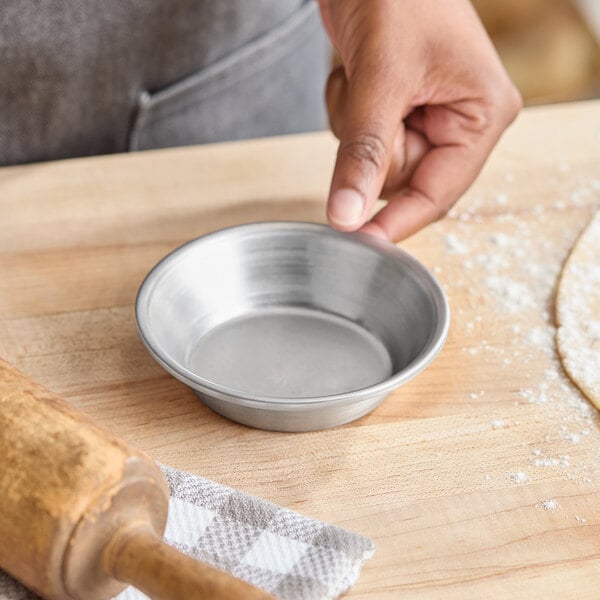 A small round aluminum pie pan on a wooden surface next to a rolling pin and dough.