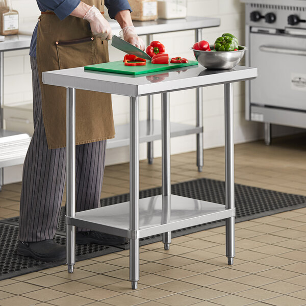 A man cutting green peppers on a Regency stainless steel work table in a professional kitchen.