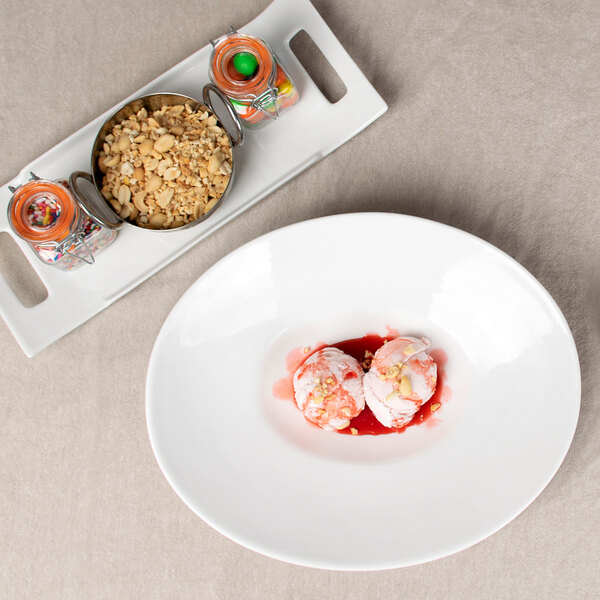 A white plate with two scoops of ice cream and red sauce in a 10 Strawberry Street Whittier shallow oval bowl.