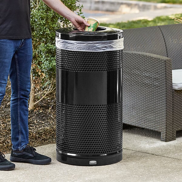 A man standing next to a black Rubbermaid round steel trash can with a rigid plastic liner.