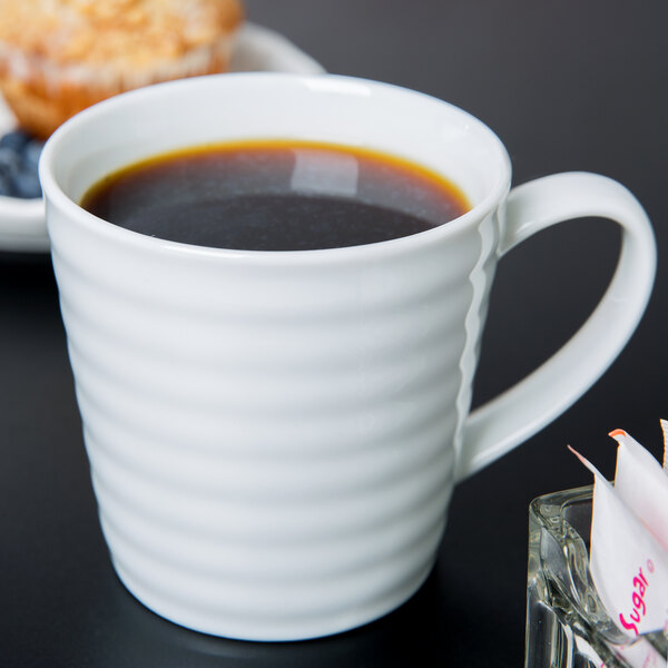 A white 10 Strawberry Street Swing porcelain mug filled with coffee on a table with a muffin.