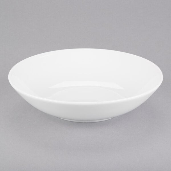An Arcoroc white coupe bowl on a gray surface.