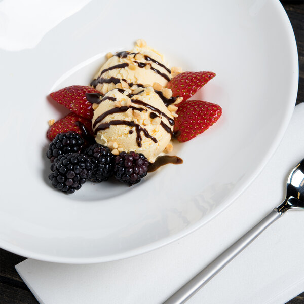 A 10 Strawberry Street Whittier white porcelain bowl filled with ice cream, berries, and chocolate sauce.