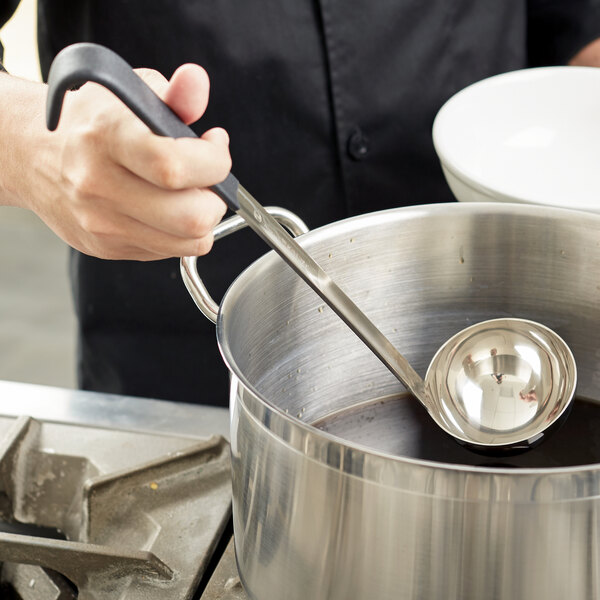 A person holding a Vollrath Jacob's Pride ladle over a pot of liquid.