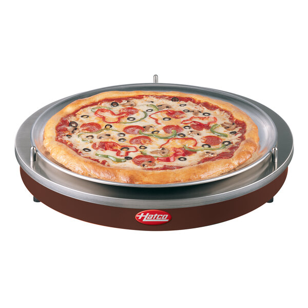 A pizza on a Hatco heated shelf on a table in a pizza parlor.