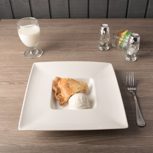 A white square porcelain bowl with a slice of pie and a ball of ice cream on a table.